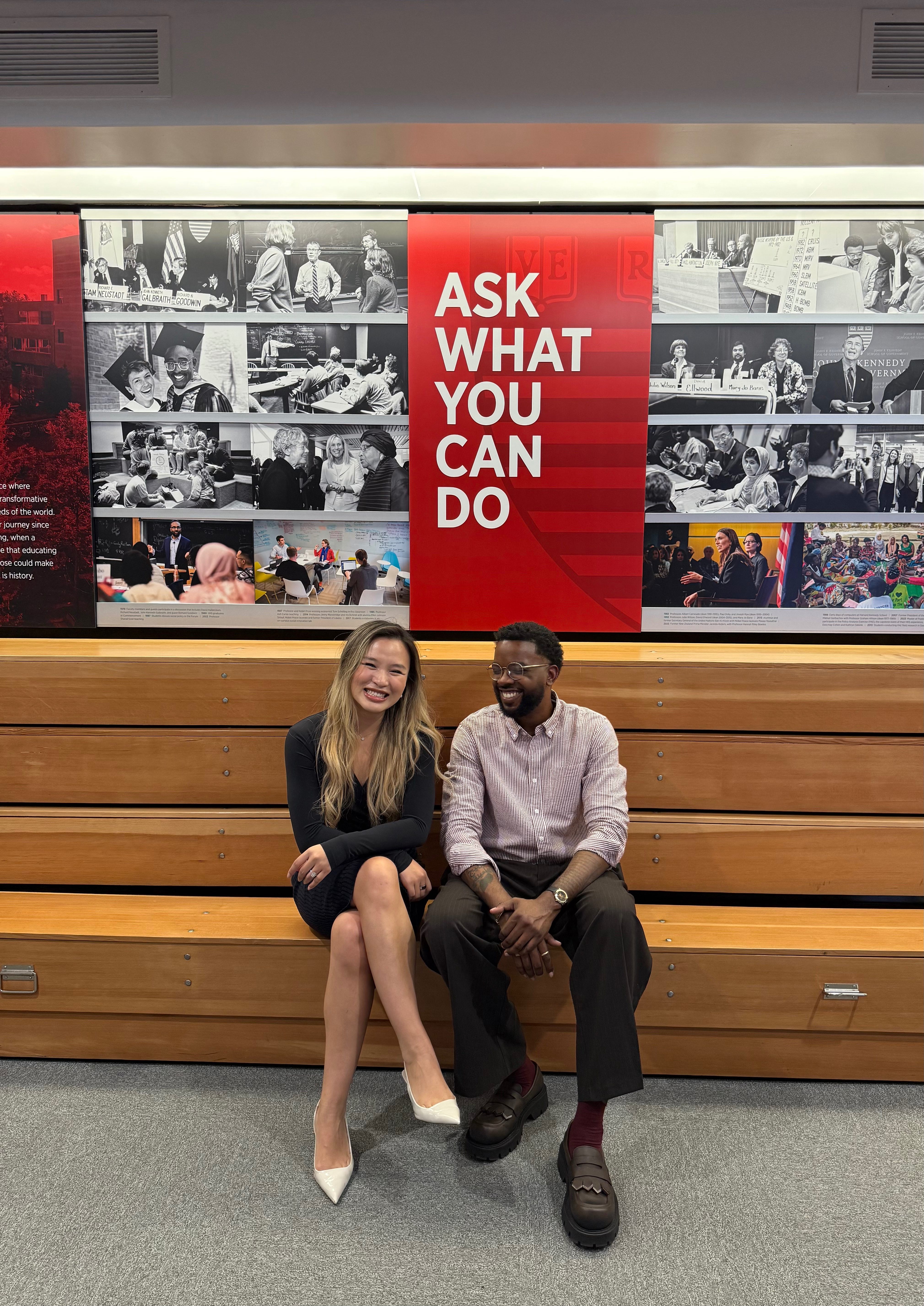 Xinyi and Andrew laughing together beneath the Harvard Kennedy School “Ask what you can do” wall.