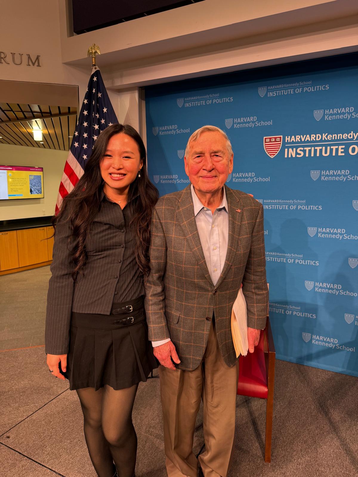 Onstage at the Institute of Politics Forum beside the U.S. flag and the Harvard Kennedy School backdrop
